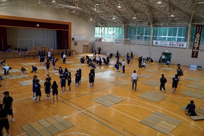 災害時に山田高校が避難所になった場合を想定した常設訓練の写真。生徒が体育館に間隔を空け畳敷きをしている。