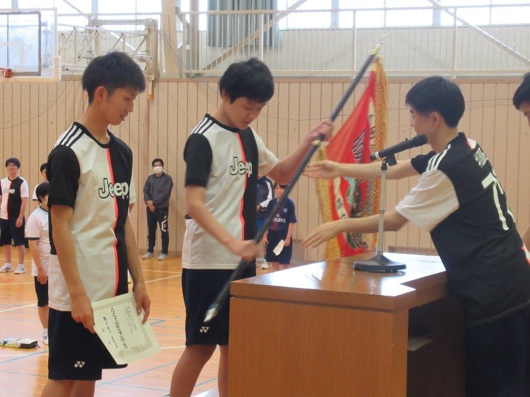 閉会式の写真。総合優勝を飾った3年Ａ組の生徒代表が賞状と優勝旗をステージで受け取っている。